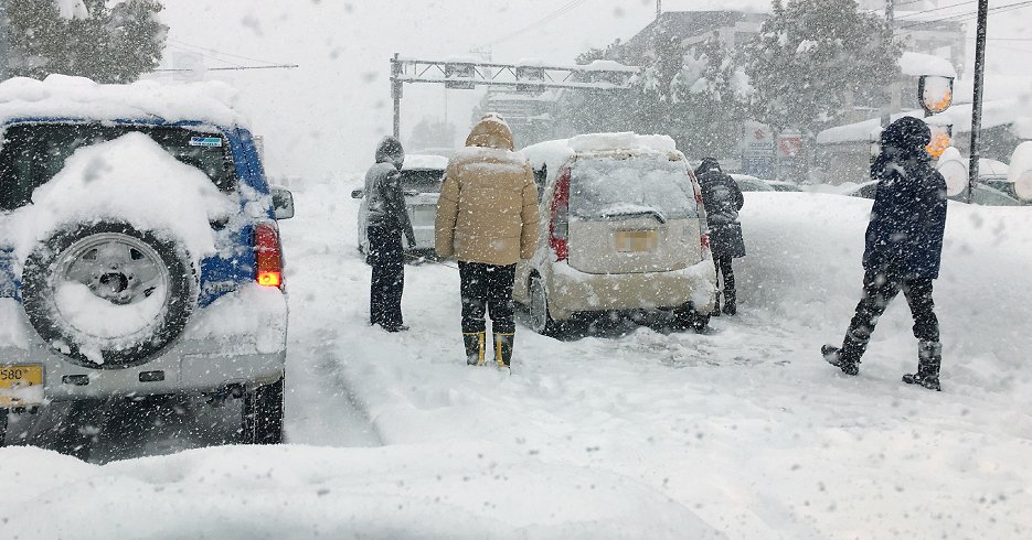 大雪で動けなくなった乗用車とドライバーら（6日、福井市内の国道8号、時事）
