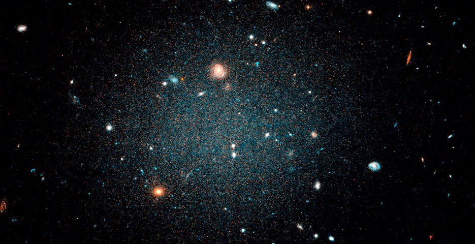 「NGC1052」と近接する銀河「DF2」は猛烈な速度で拡散しているため、その後ろに存在する遠くの銀河をはっきりと確認することができる。暗黒物質のすべてではないにしても、そのほとんどが存在しないと結論づけた（ハッブル宇宙望遠鏡で撮影、写真提供：NASA、ESA、P. van Dokkum [エール大学]）
